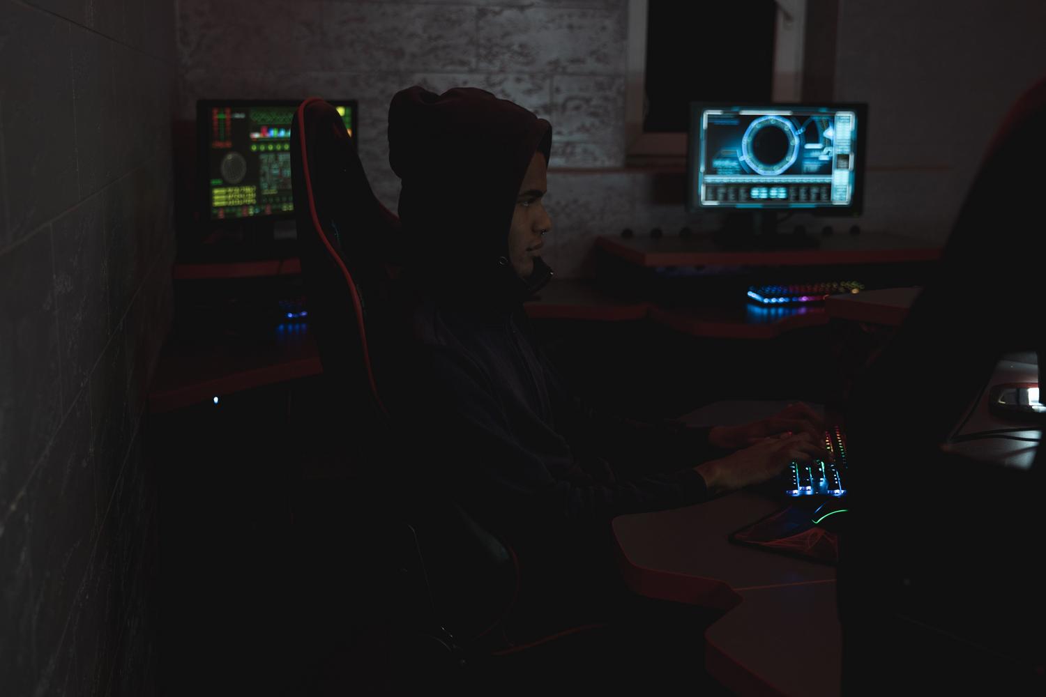 Cybersecurity analyst monitoring multiple screens in a dark room, illustrating the cognitive load of alert correlation.