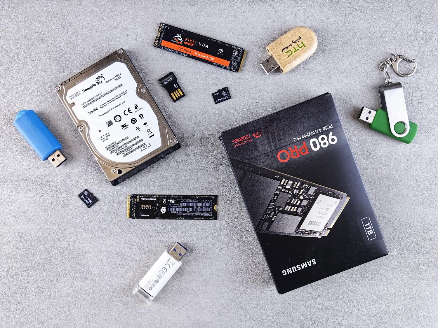 Vista cenital de diversos dispositivos de almacenamiento de datos modernos y antiguos, incluyendo HDD y SSD, dispuestos sobre una superficie gris tecnológica. Vista cenital de diversos dispositivos de almacenamiento de datos modernos y antiguos, incluyendo HDD y SSD, dispuestos sobre una superficie gris tecnológica.