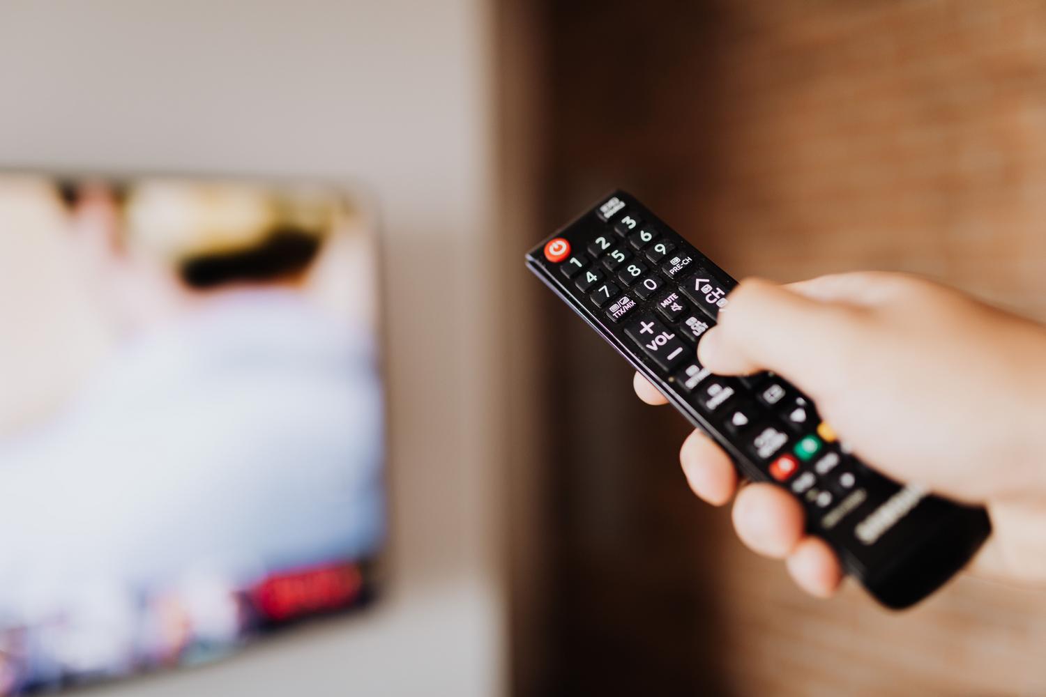 Detalle de una mano sosteniendo un mando a distancia de televisión para navegar por los menús de ajustes. Detalle de una mano sosteniendo un mando a distancia de televisión para navegar por los menús de ajustes.