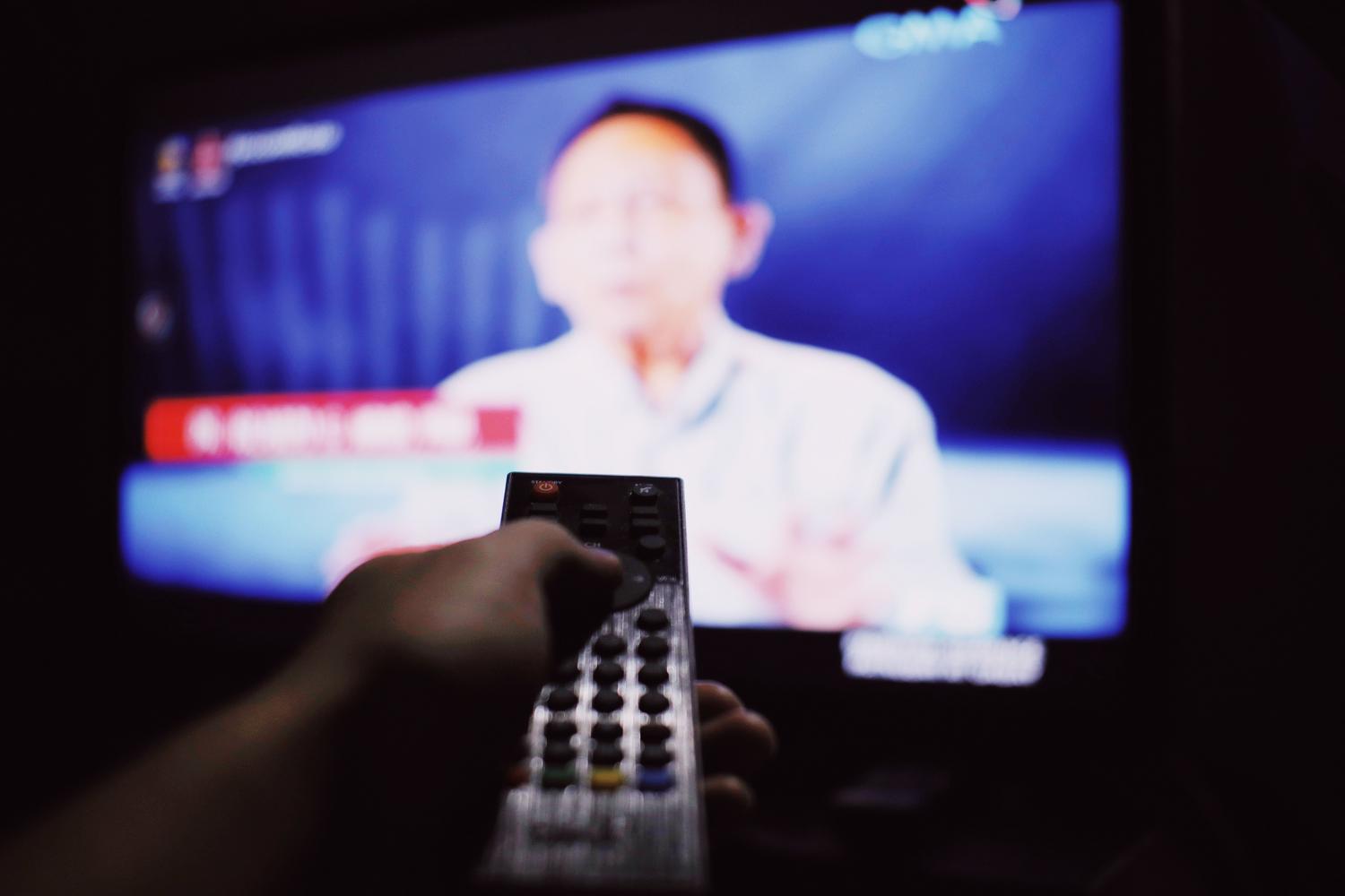 Persona cambiando de canal con el mando a distancia frente a una pantalla de televisión.