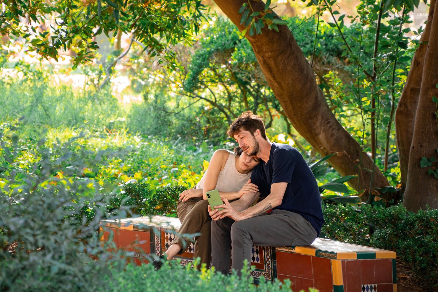 Pareja compartiendo la pantalla de un móvil en un parque soleado, sugiriendo una experiencia de juego cooperativo en Pokémon GO