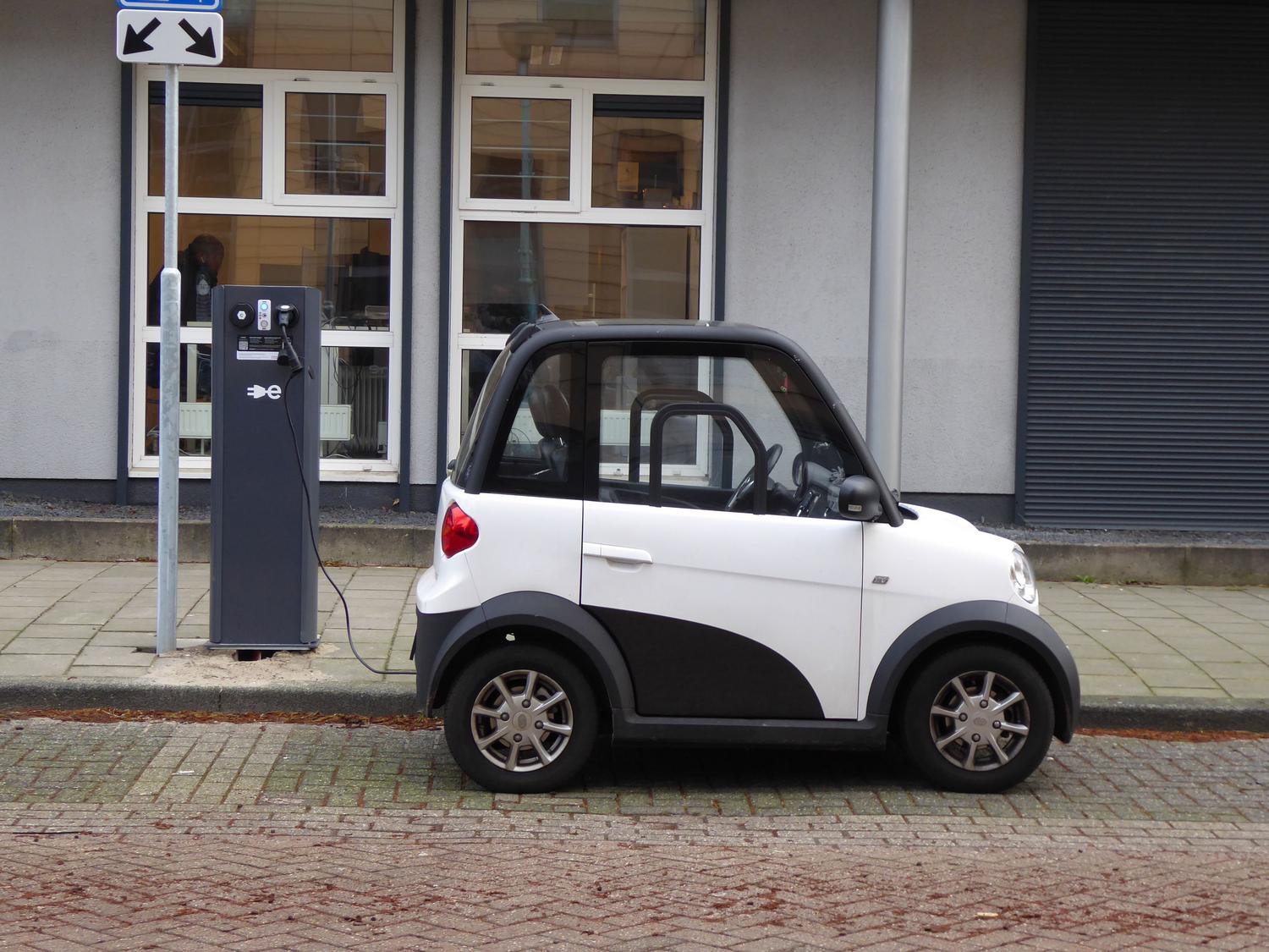 Coche eléctrico compacto cargándose en una estación de carga pública, representando la movilidad sostenible y la etiqueta 0 emisiones.