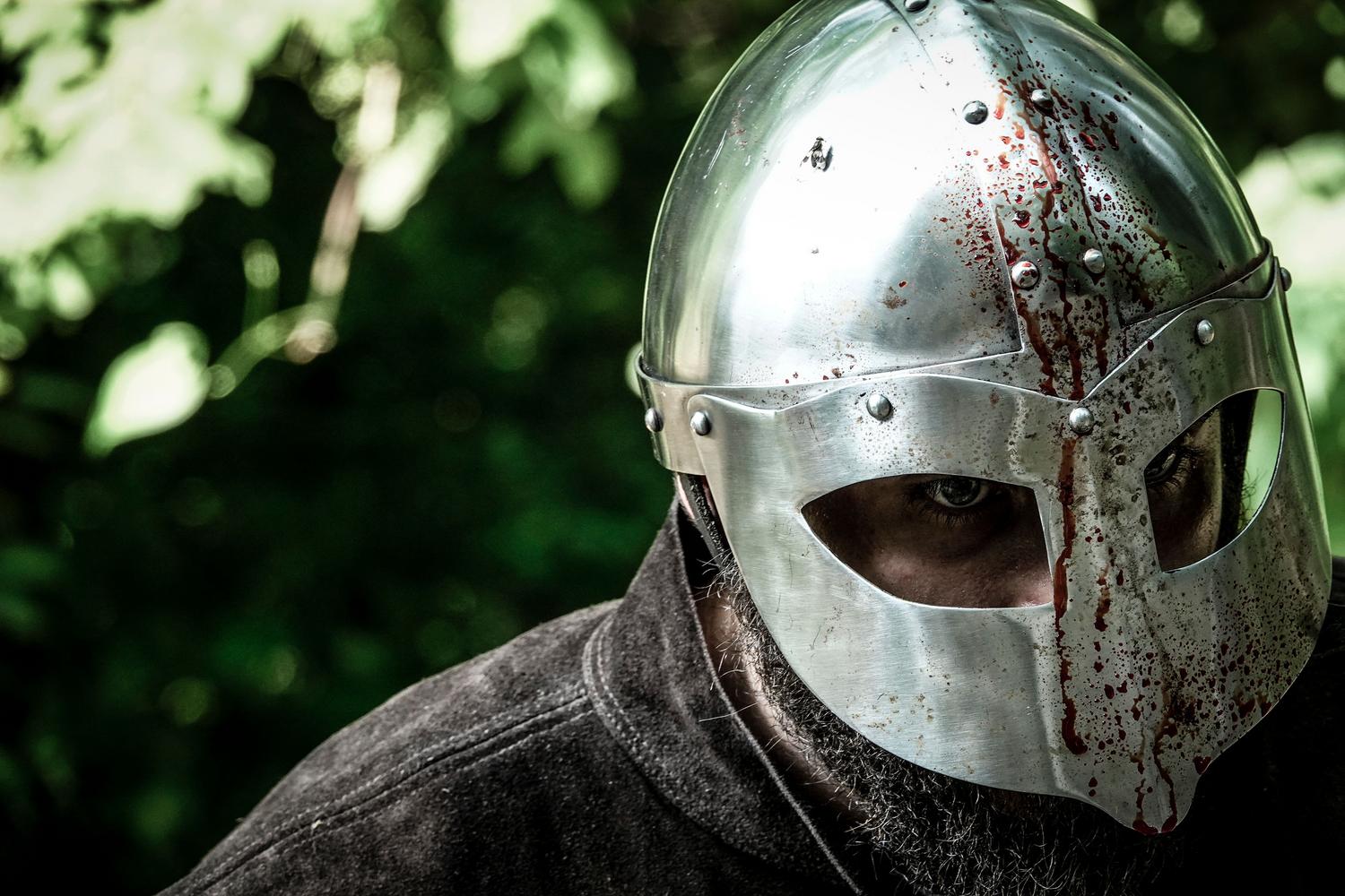 Primer plano de un casco de caballero manchado de sangre, simbolizando la persistencia y el ciclo de muerte en el juego.