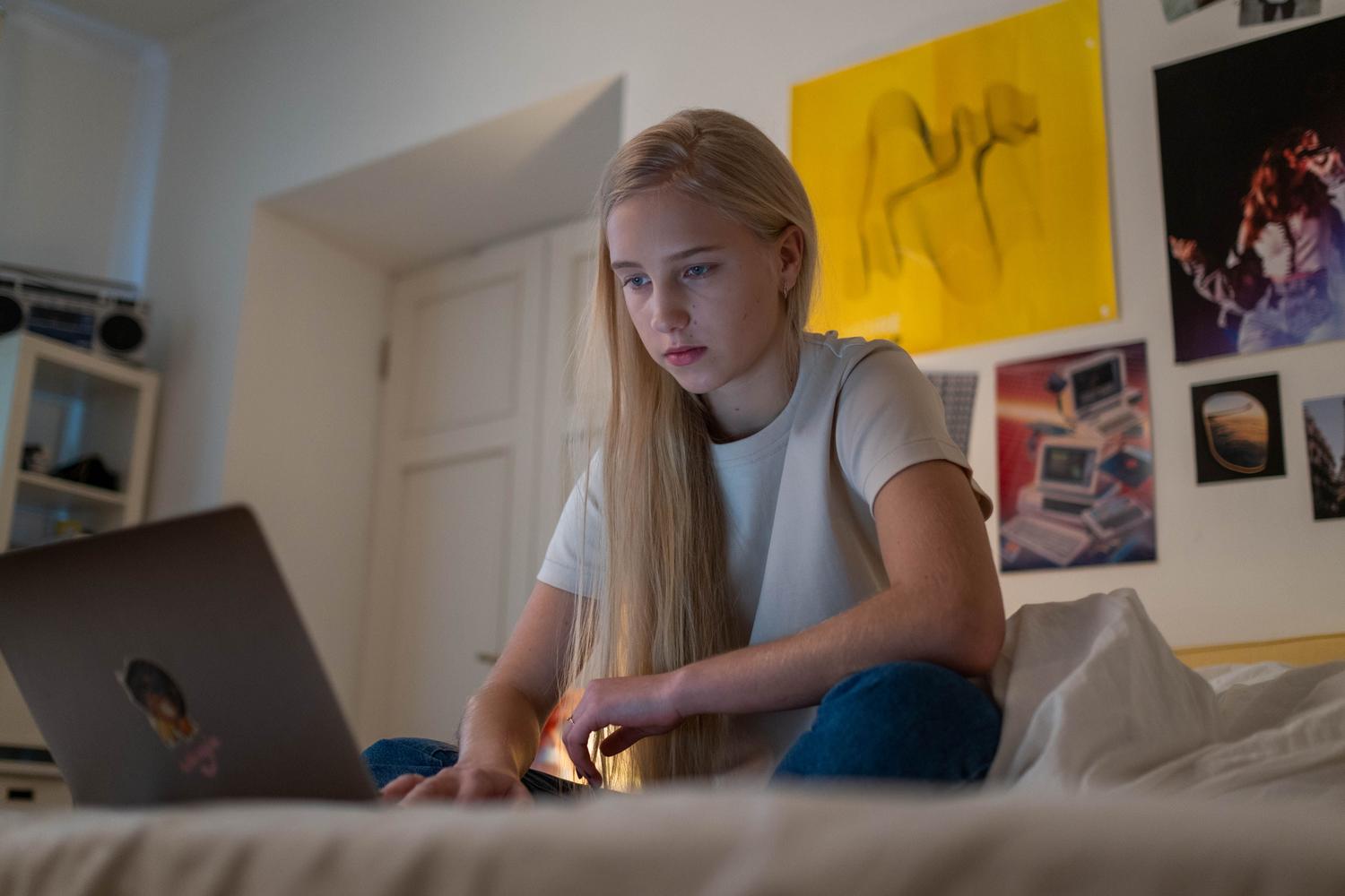Adolescente concentrada utilizando un ordenador portátil en su habitación para estudiar