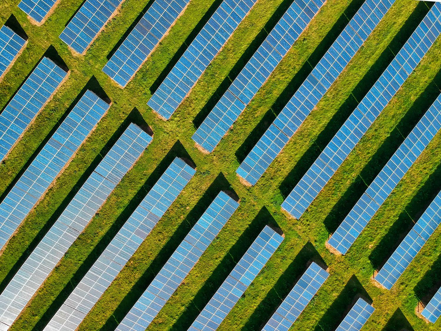 Vista aérea de una planta de paneles solares en un campo verde, simbolizando el uso de energías renovables. Vista aérea de una planta de paneles solares en un campo verde, simbolizando el uso de energías renovables.