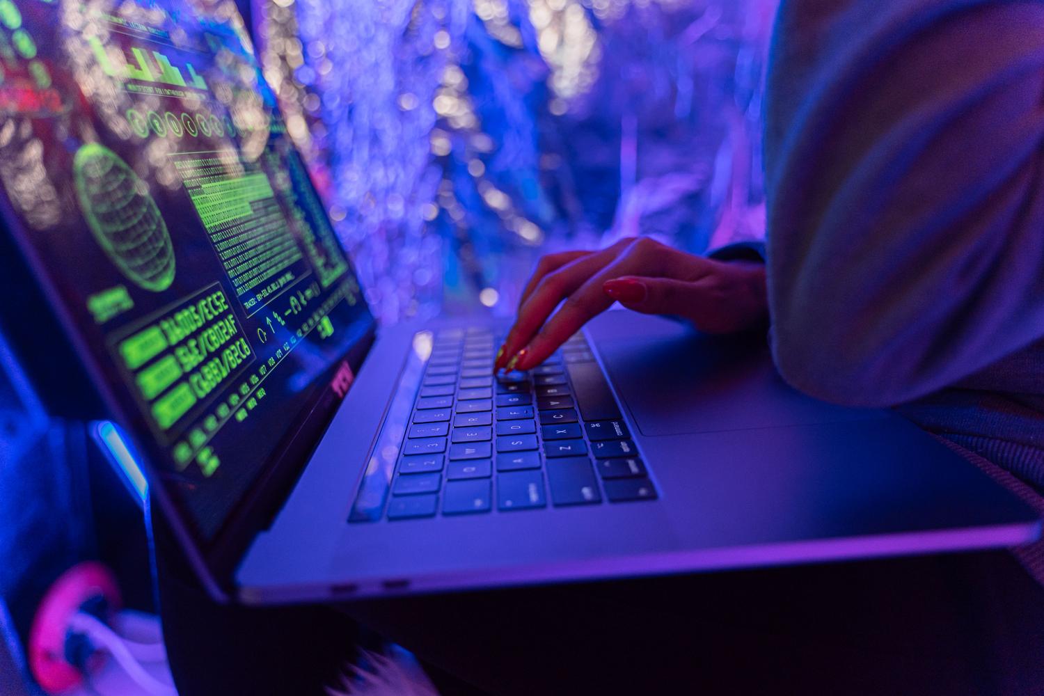 Manos configurando parámetros de seguridad en una laptop con gráficos de ciberseguridad en pantalla.