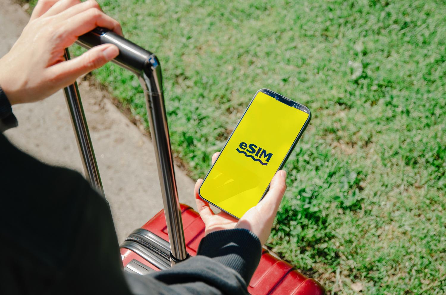 Persona sosteniendo un smartphone que muestra el texto eSIM mientras lleva una maleta roja, ilustrando la facilidad de usar eSIM al viajar.