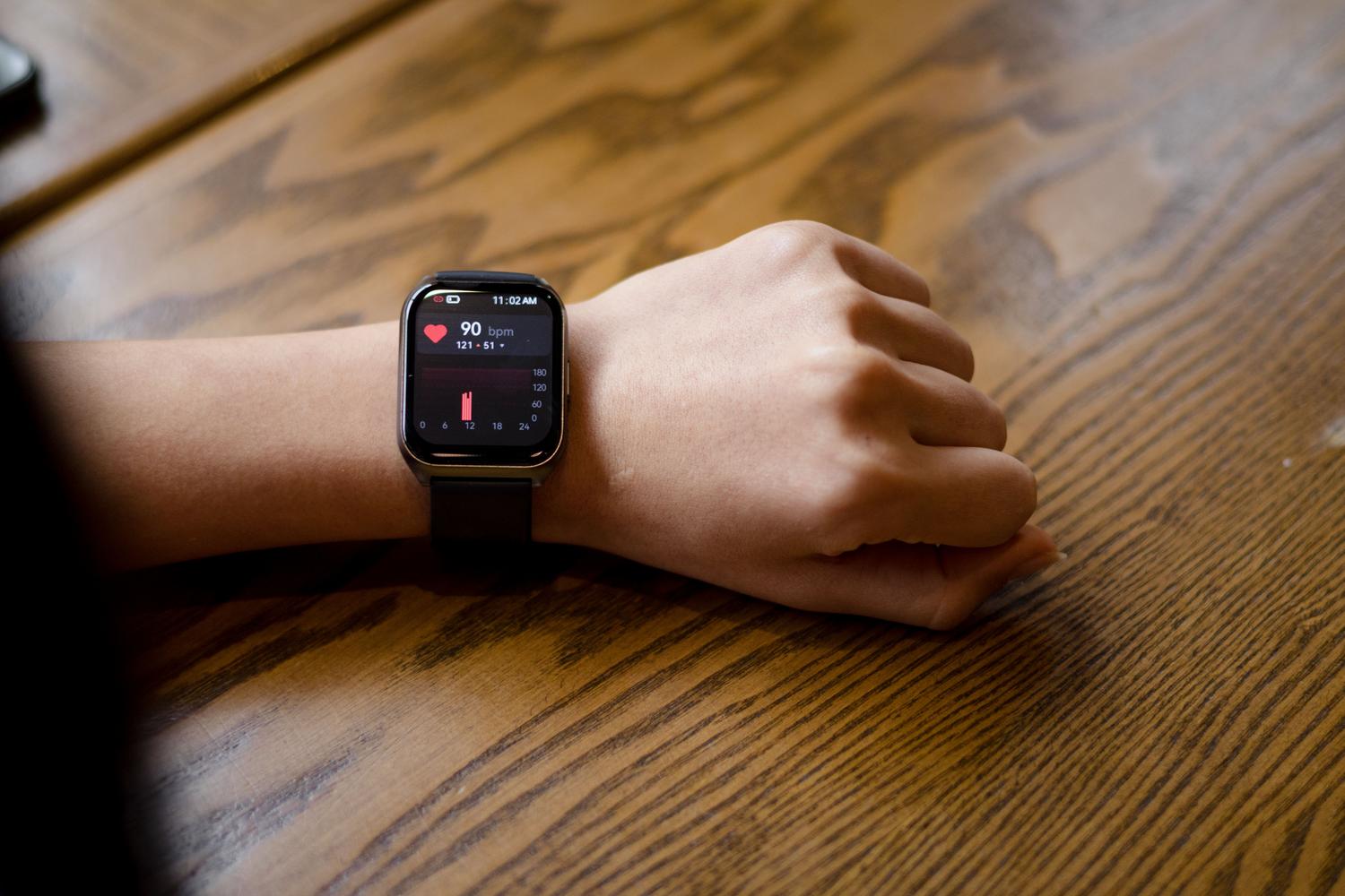 Primer plano de un smartwatch mostrando la frecuencia cardíaca en la muñeca de una persona, ejemplificando el uso de wearables en la medicina proactiva.