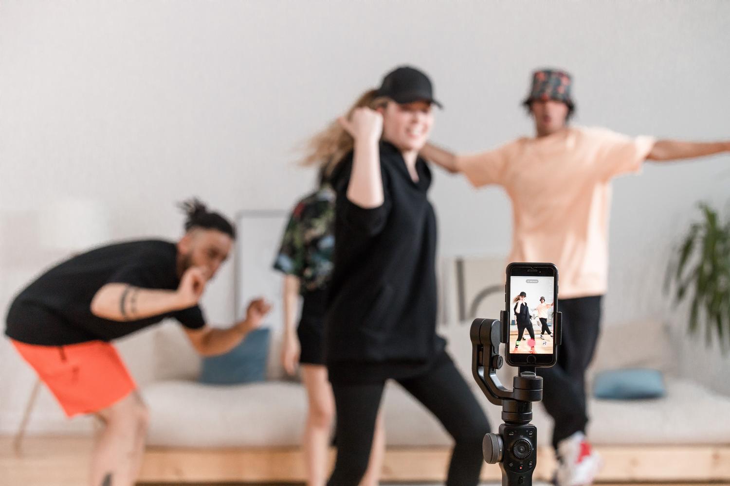 Grupo de jóvenes bailando para crear contenido de TikTok utilizando un smartphone con estabilizador.