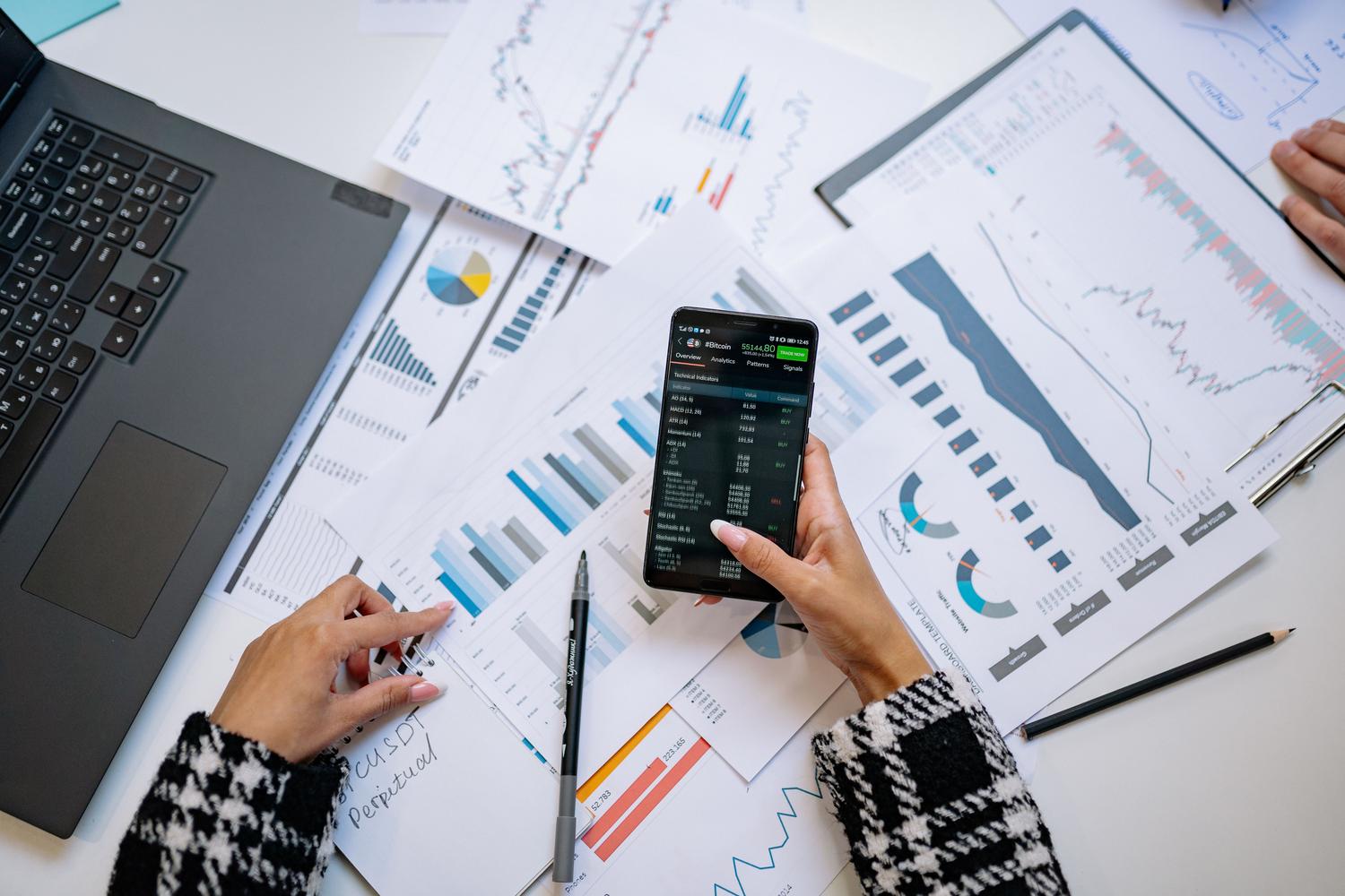 Escritorio de trabajo con gráficos impresos y un smartphone mostrando datos en tiempo real para el análisis de tendencias.