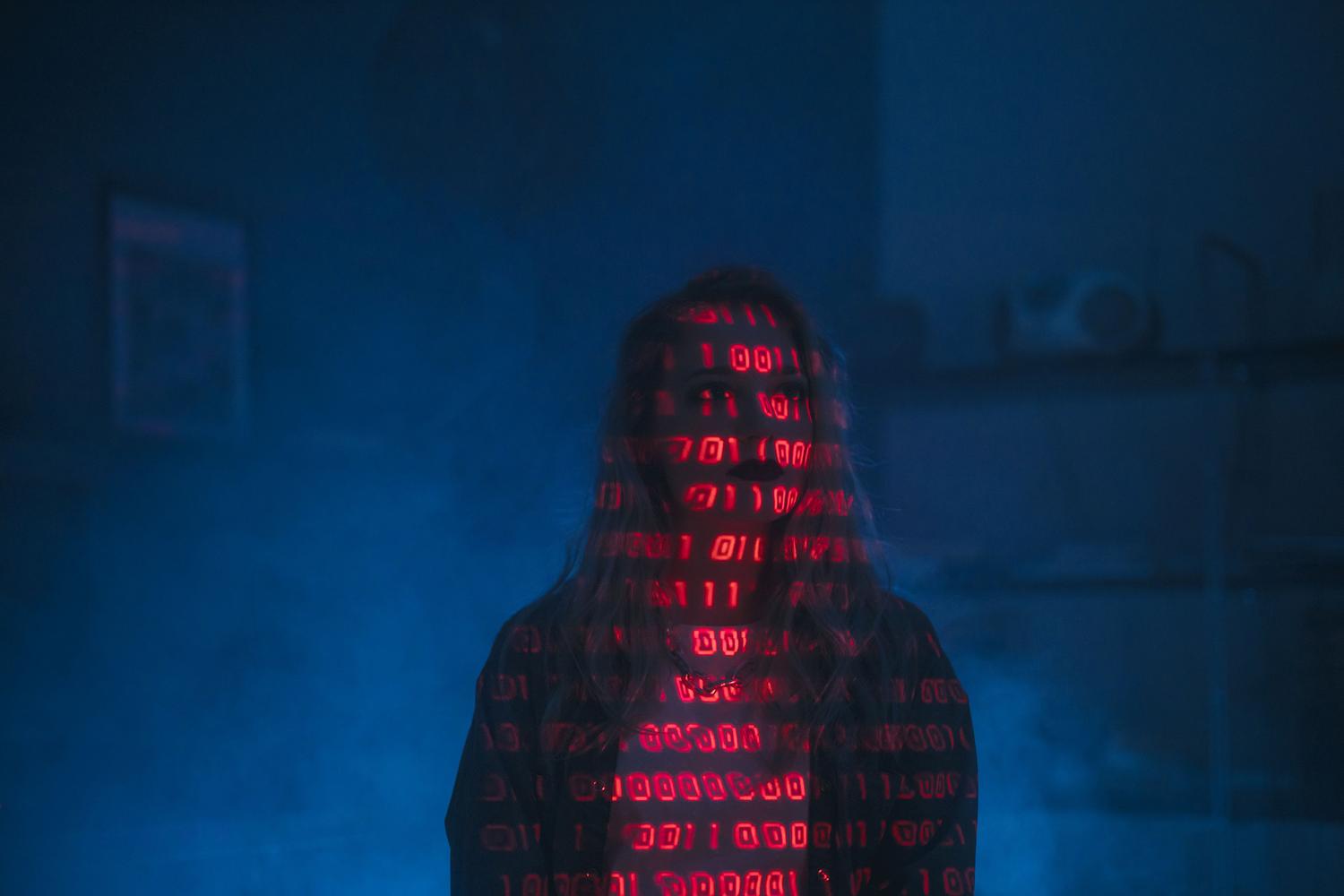 Mujer con código binario rojo proyectado sobre su rostro, representando ataques adversarios y envenenamiento de datos en modelos de IA.