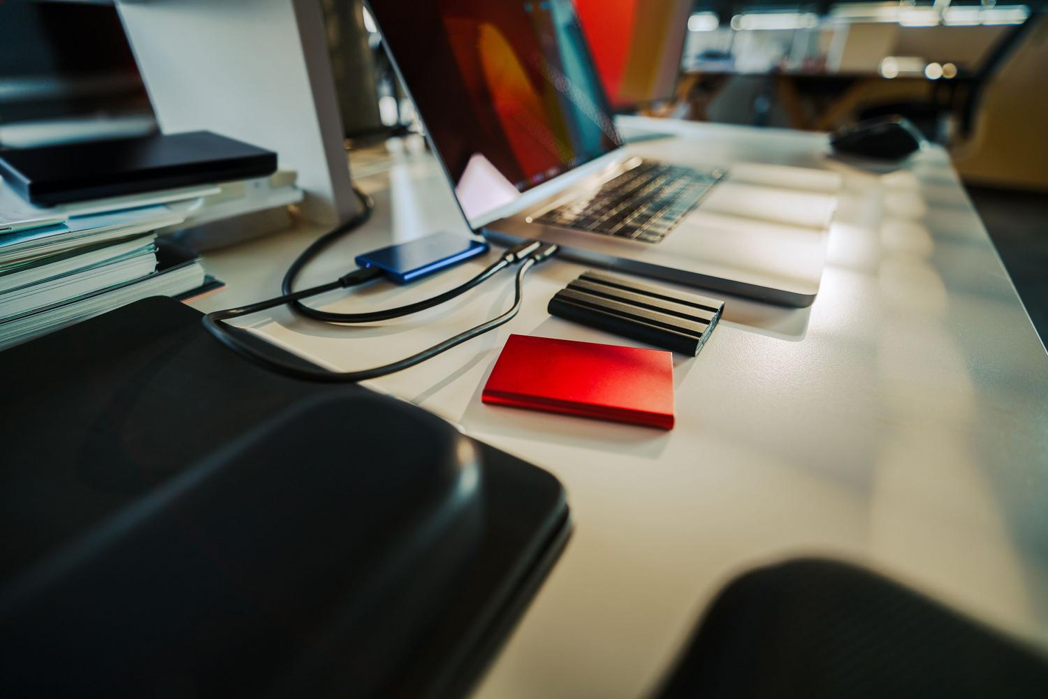 Escritorio de oficina con un portátil y múltiples discos duros externos, representando una estrategia de redundancia y supervivencia digital.