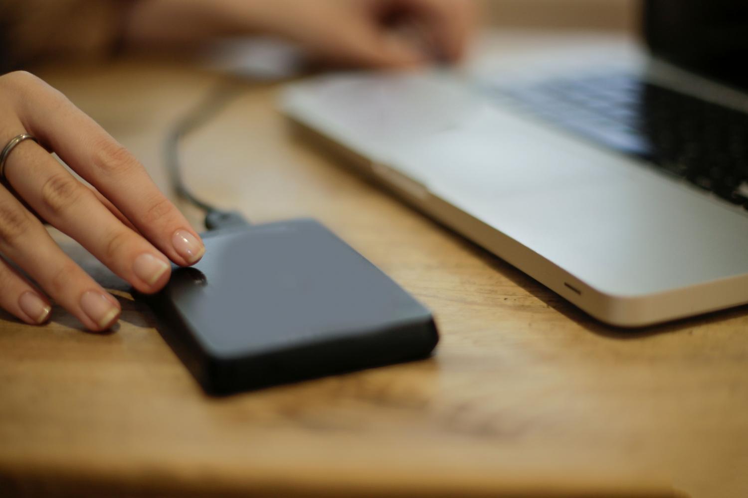 Persona conectando un disco duro externo a un ordenador portátil para realizar una copia de seguridad de sus archivos.
