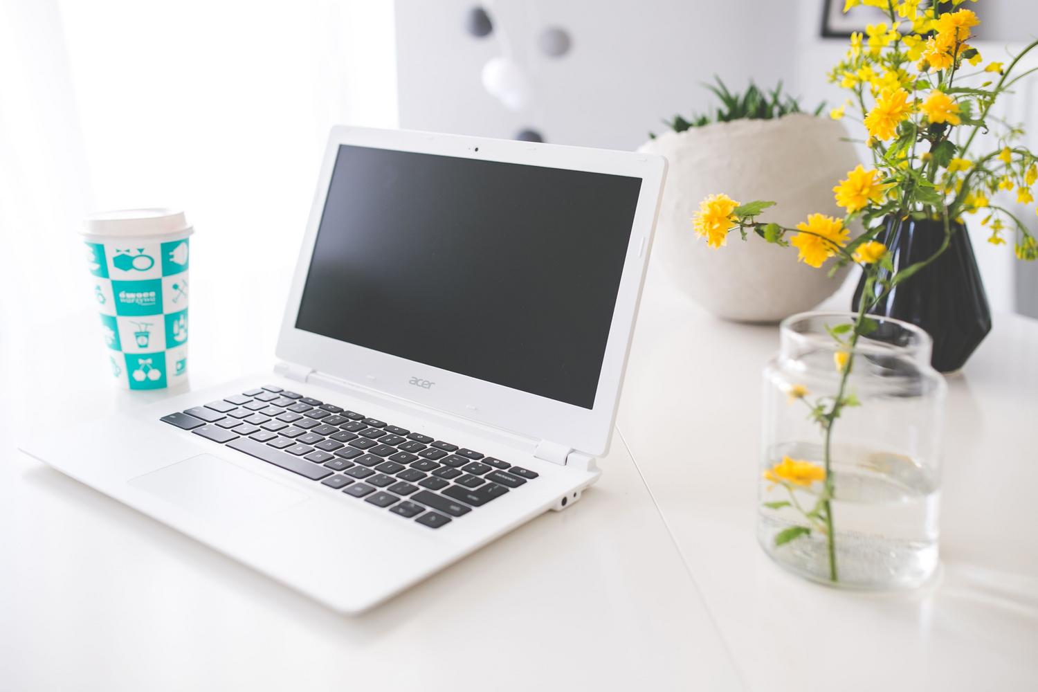 Chromebook Acer en un escritorio blanco y luminoso con café y flores, ideal para representar el uso en casa.
