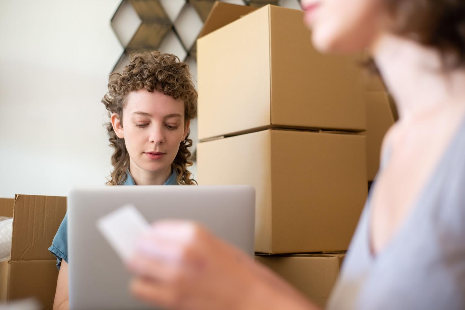 Dueña de tienda online gestionando pedidos desde su portátil rodeada de cajas, reflejando la intensidad de la campaña de Black Friday.
