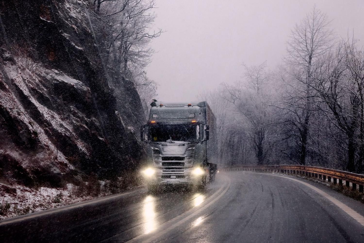 Camión pesado transitando por una carretera de montaña nevada con efectos de lluvia y nieve.