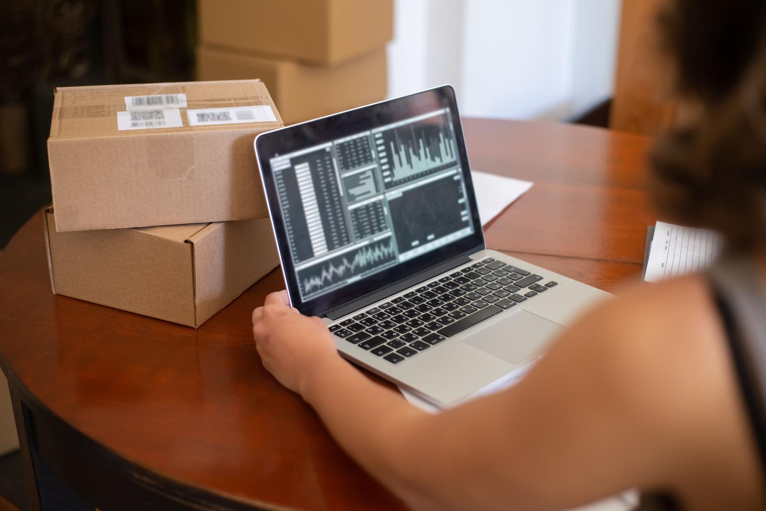 Emprendedor gestionando pedidos online con laptop y cajas de envío, ilustrando la gestión operativa y logística de Amazon FBA.