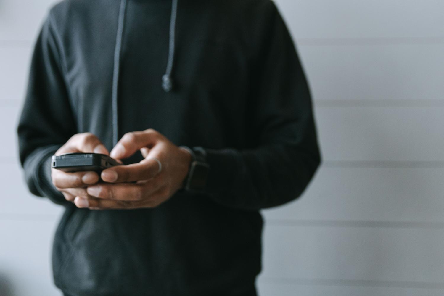 Persona con sudadera negra usando un teléfono inteligente en un entorno interior casual y luminoso.