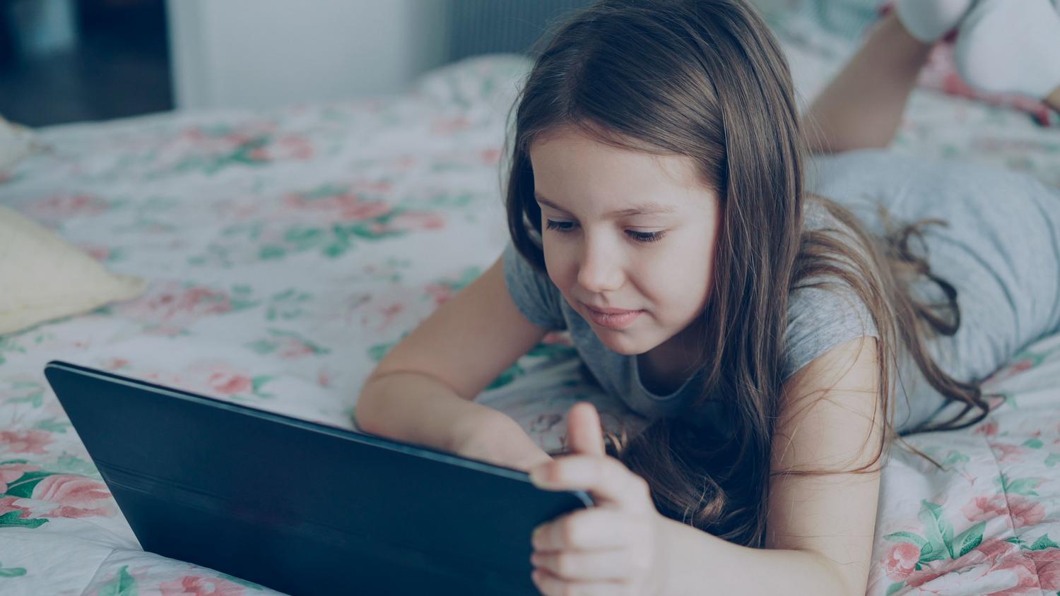 Una niña utilizando una tablet en la intimidad de su habitación, representando el espacio personal donde los menores interactúan con la red.