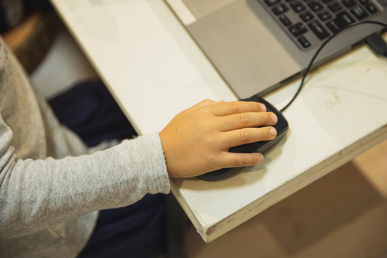 Primer plano de un estudiante utilizando un ratón de ordenador en el aula, representando la alfabetización mediática y la educación digital escolar.