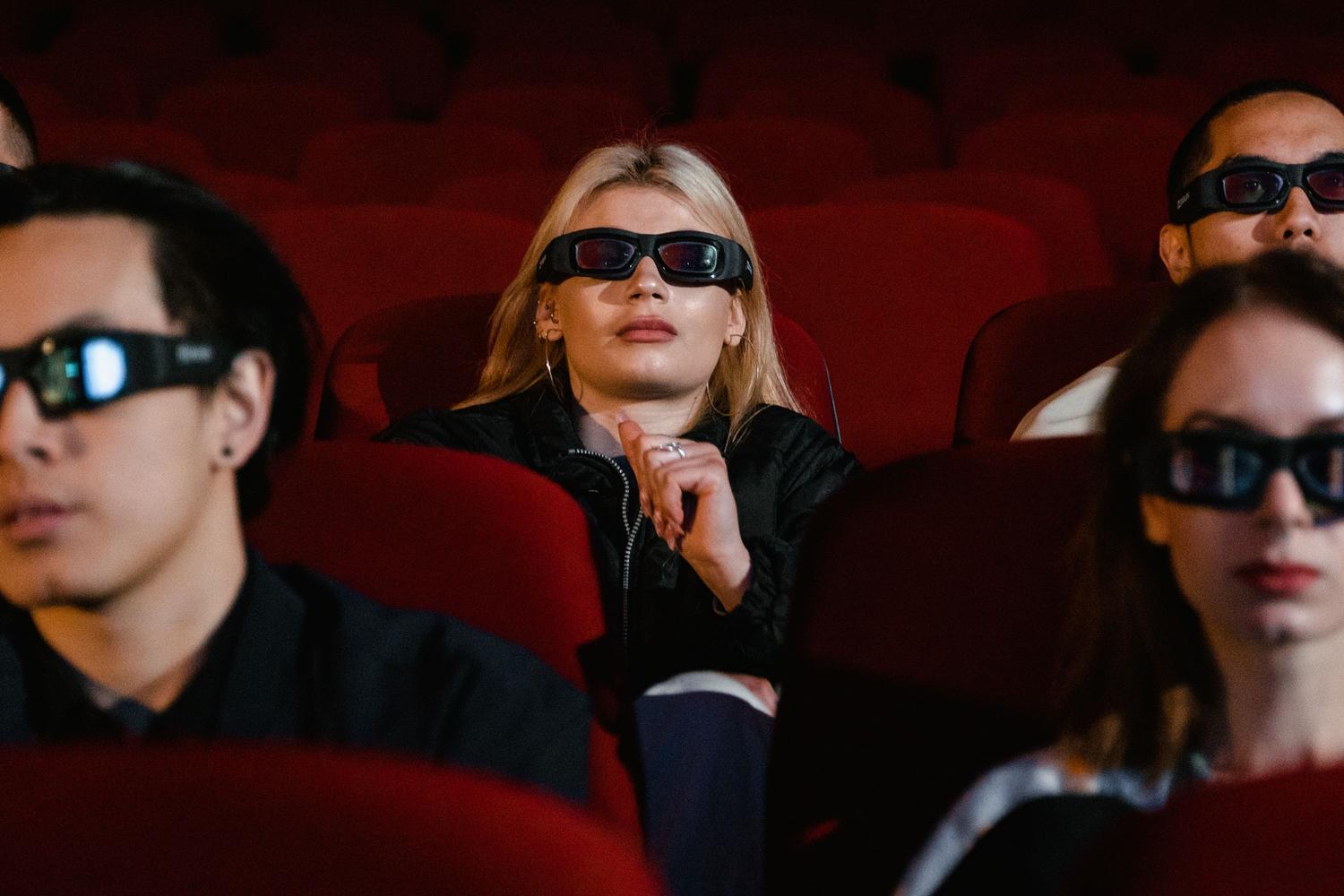 Espectadores con gafas 3D en una sala de cine, relacionando la experiencia visual con los requisitos técnicos de luminosidad en 3D.