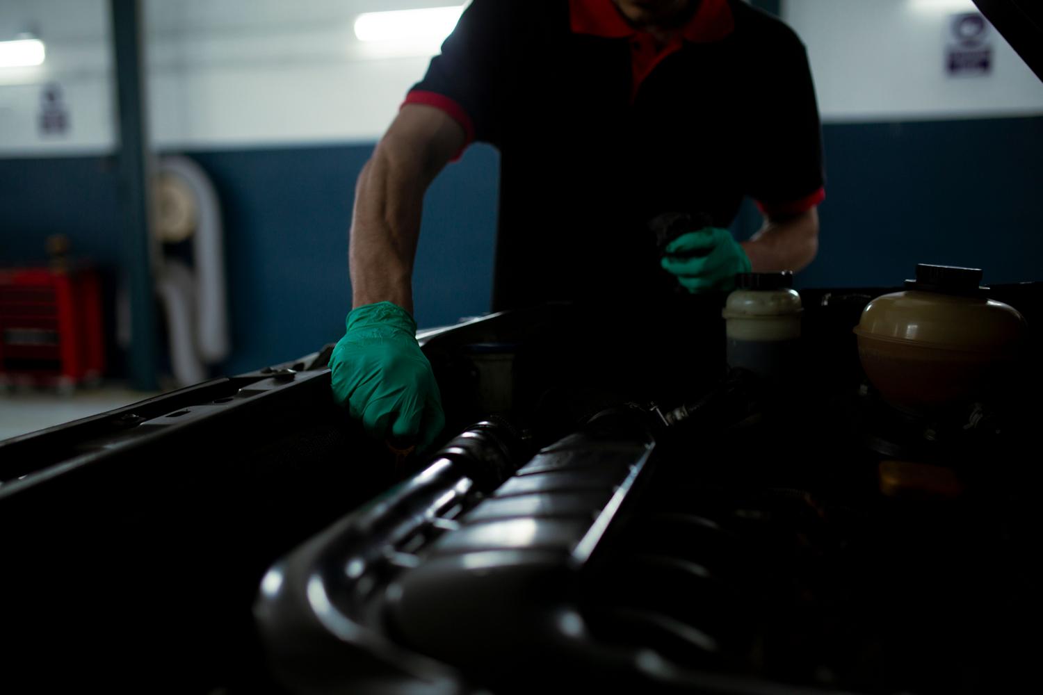 Técnico automotriz realizando una inspección técnica del motor de un coche en un garaje iluminado