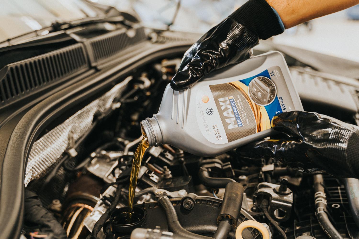 Mecánico vertiendo aceite nuevo en el motor de un coche para su mantenimiento regular