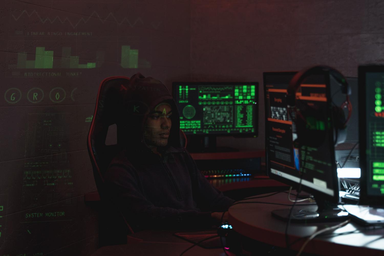 Un hacker con capucha monitoreando múltiples pantallas en un entorno oscuro, ilustrando la amenaza del robo de cookies y el secuestro de sesión.
