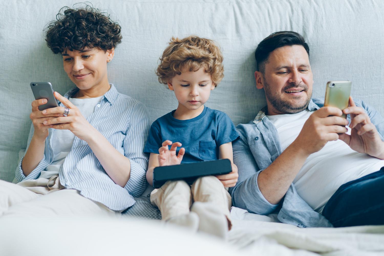Familia disfrutando del uso simultáneo de diversos dispositivos digitales en el sofá de su casa.