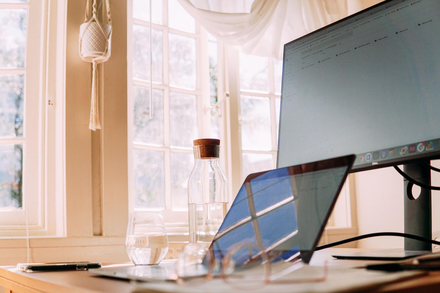 Espacio de trabajo en casa moderno con ordenador y monitor, iluminado con luz natural.