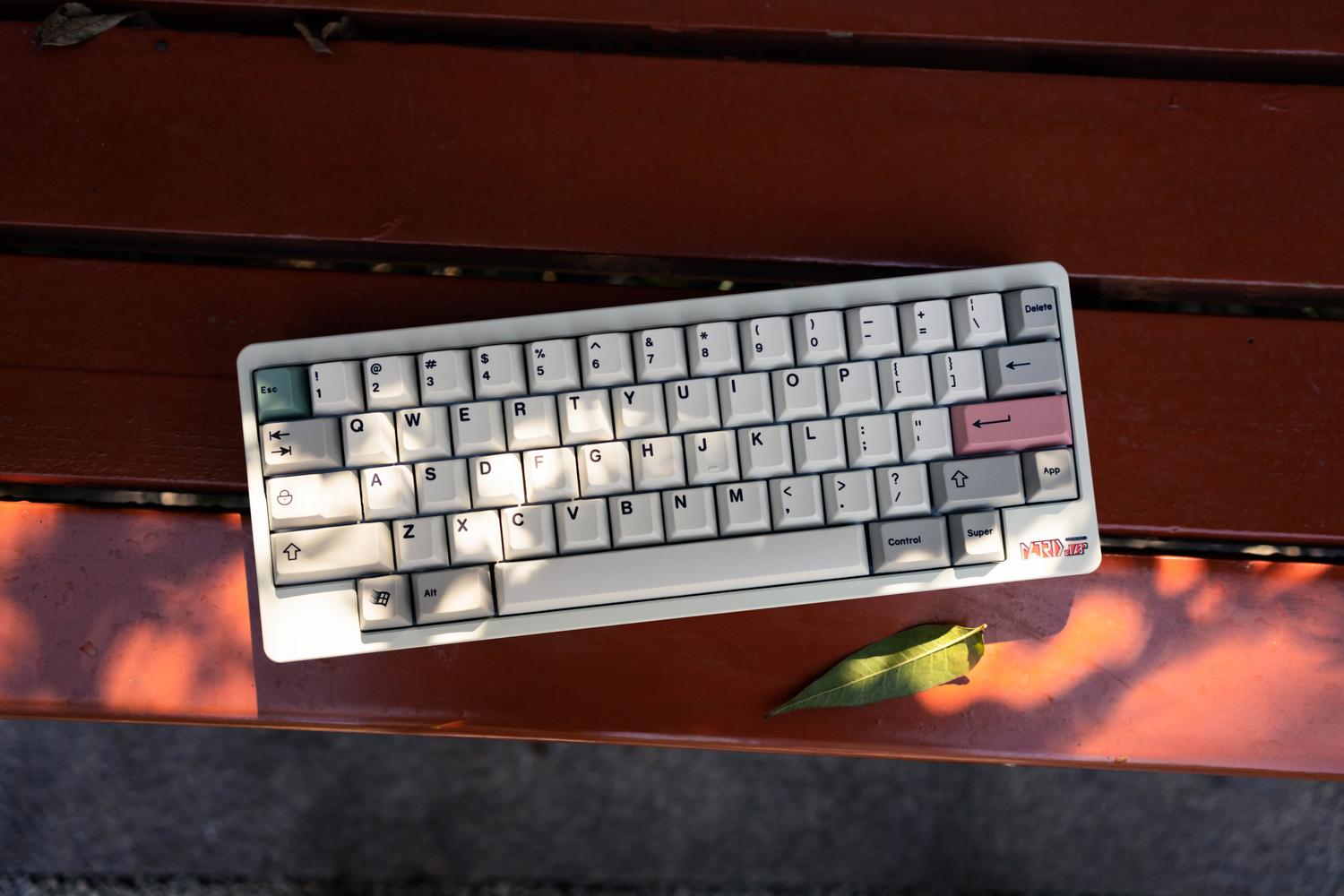 Teclado mecánico inalámbrico blanco de formato compacto sobre una superficie de madera natural.