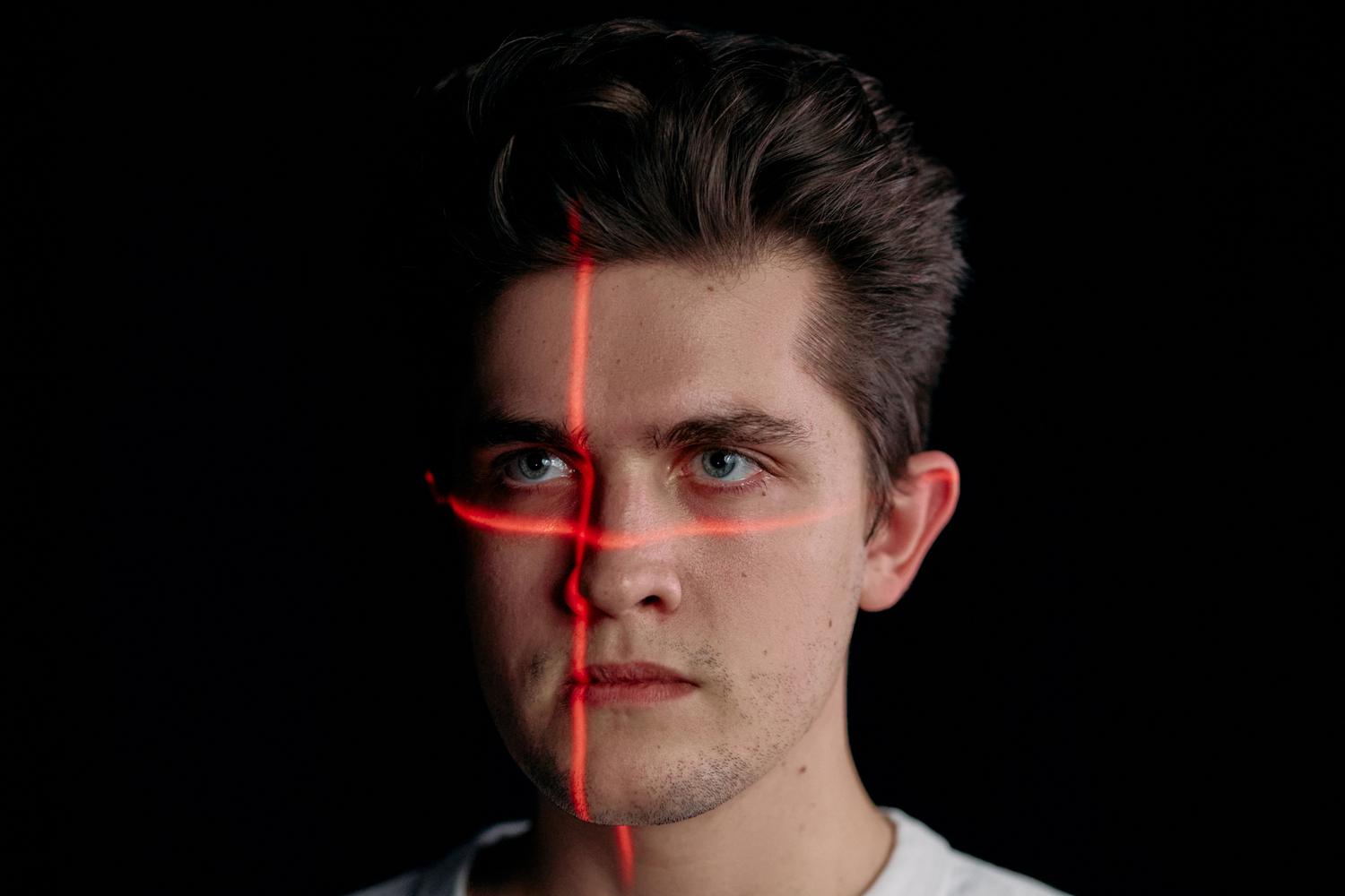 Retrato conceptual de un hombre con líneas de escaneo láser en el rostro, representando la tecnología de análisis biométrico facial para la verificación de identidad.