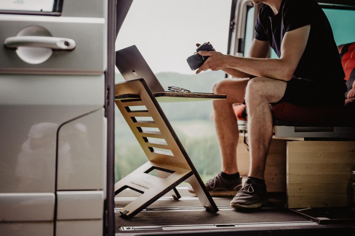 Hombre teletrabajando desde su furgoneta camper con un equipo de oficina portátil, ilustrando la disciplina del trabajo remoto en espacios reducidos. Hombre teletrabajando desde su furgoneta camper con un equipo de oficina portátil, ilustrando la disciplina del trabajo remoto en espacios reducidos.