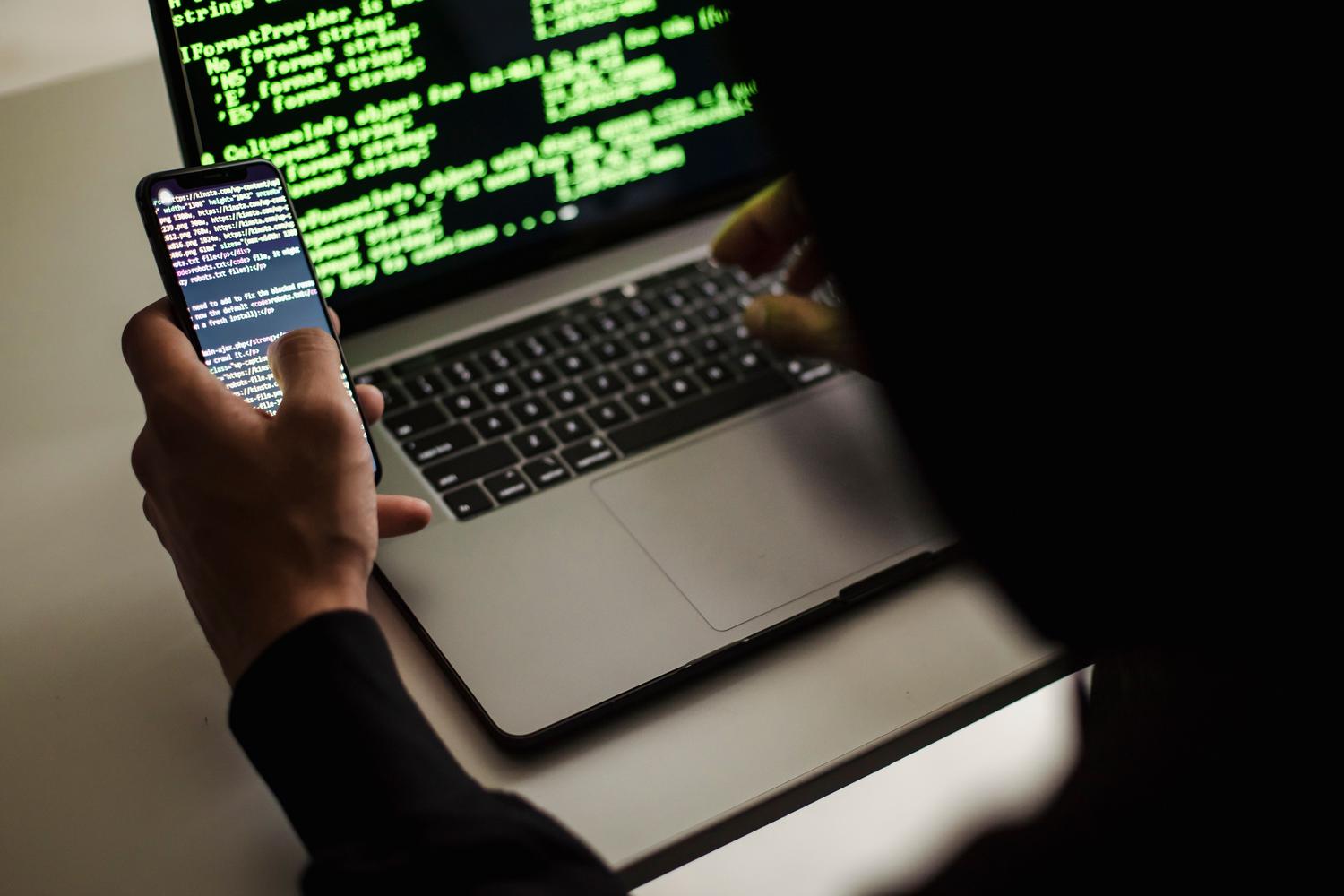 Desarrollador utilizando simultáneamente un ordenador portátil y un teléfono móvil para depuración de software.