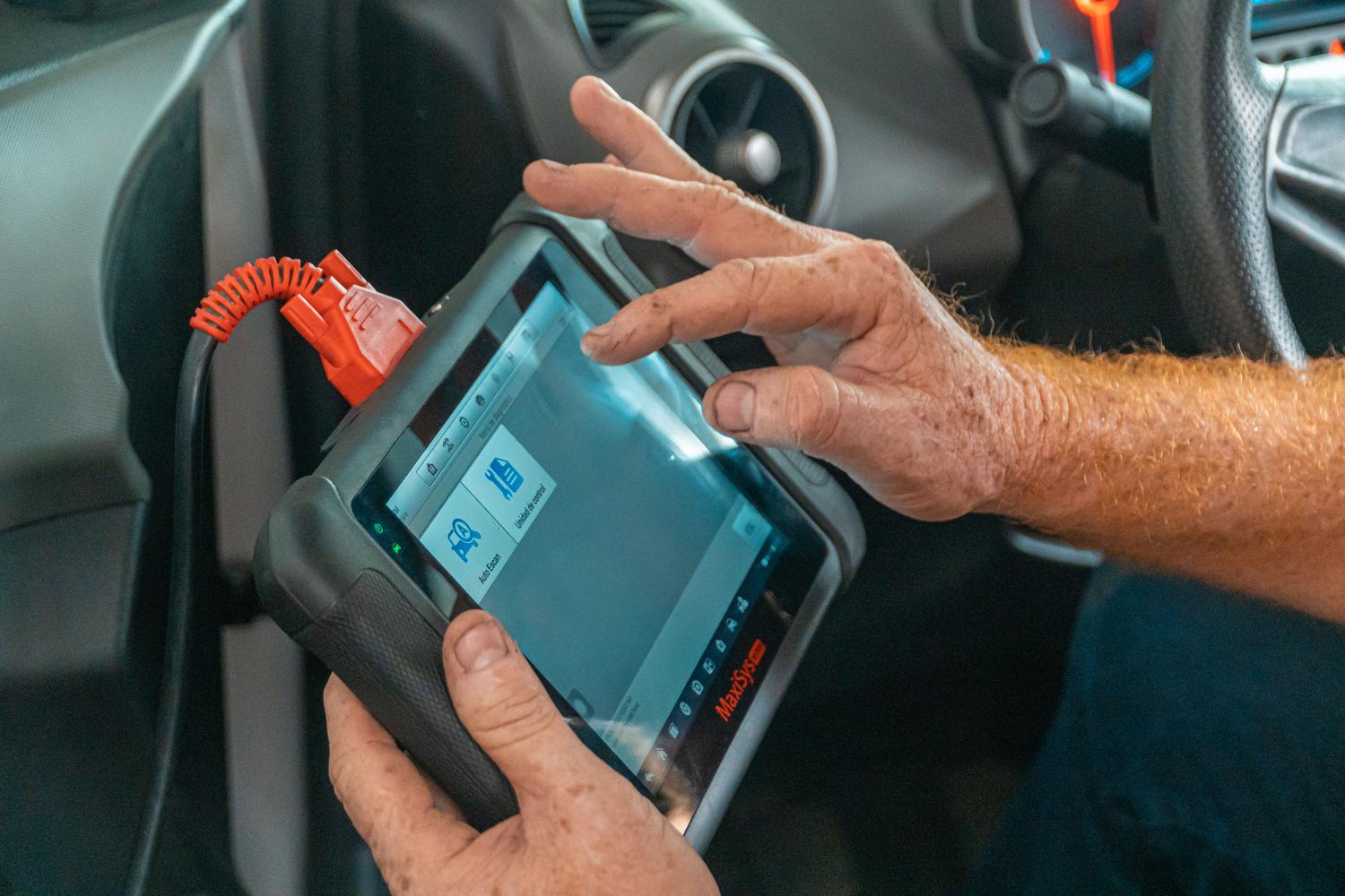 Mecánico profesional utilizando una tableta de diagnosis avanzada OBD2 para analizar fallos electrónicos en el sistema de dirección de un vehículo.