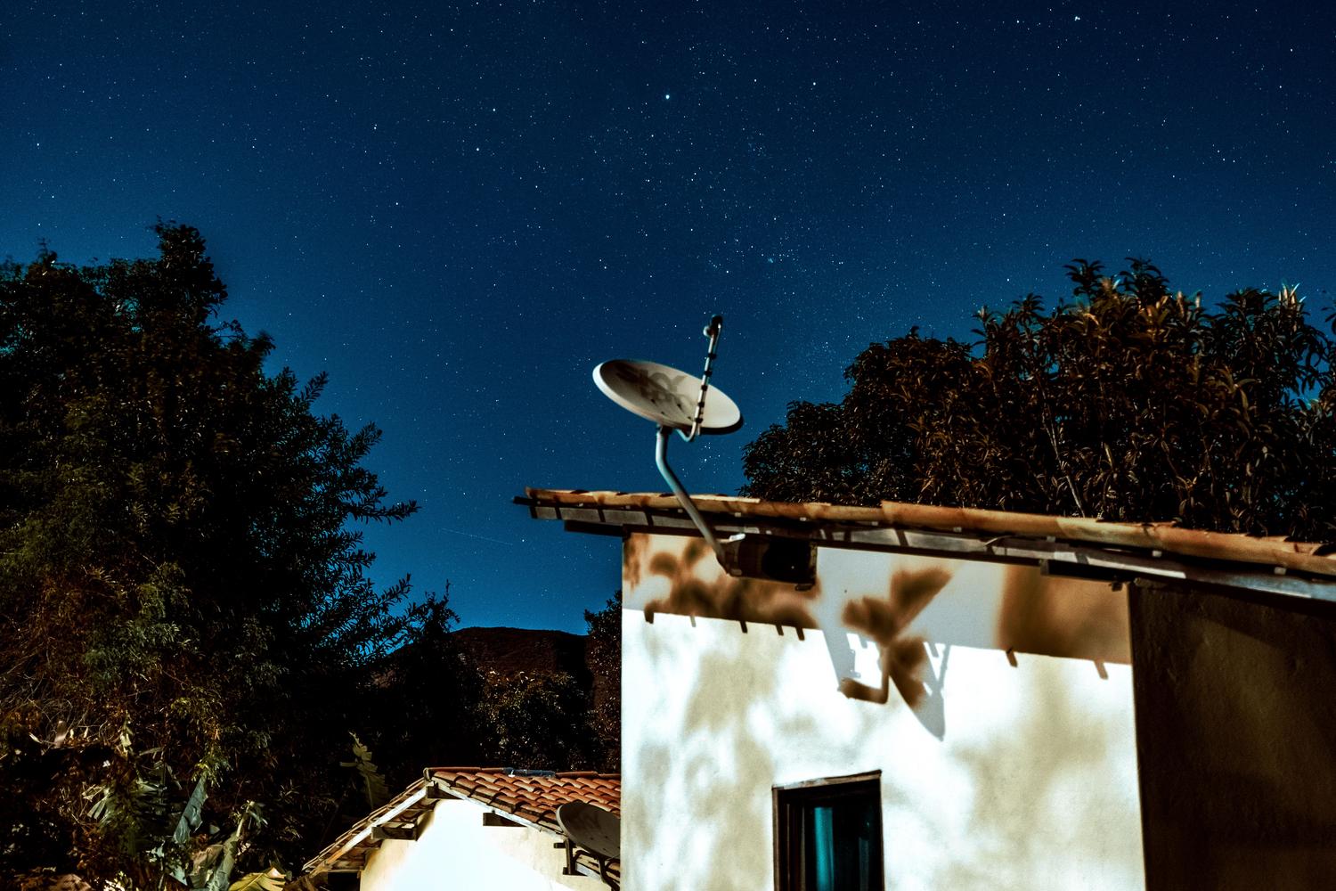 Casa rural con antena satelital bajo un cielo estrellado, simbolizando el acceso a la red global en zonas remotas.