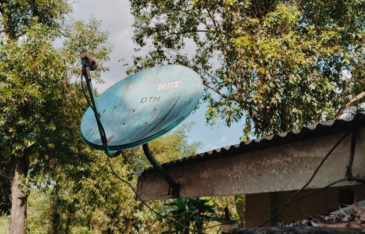 Antena parabólica instalada en el tejado de una casa rural rodeada de vegetación, capturando la esencia de la conectividad rural.