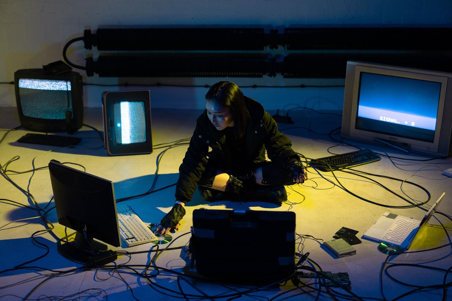 Un hacker trabajando en la penumbra rodeado de monitores antiguos y cables, representando el sigilo informativo y la lucha contra el sistema desde las sombras. Un hacker trabajando en la penumbra rodeado de monitores antiguos y cables, representando el sigilo informativo y la lucha contra el sistema desde las sombras.
