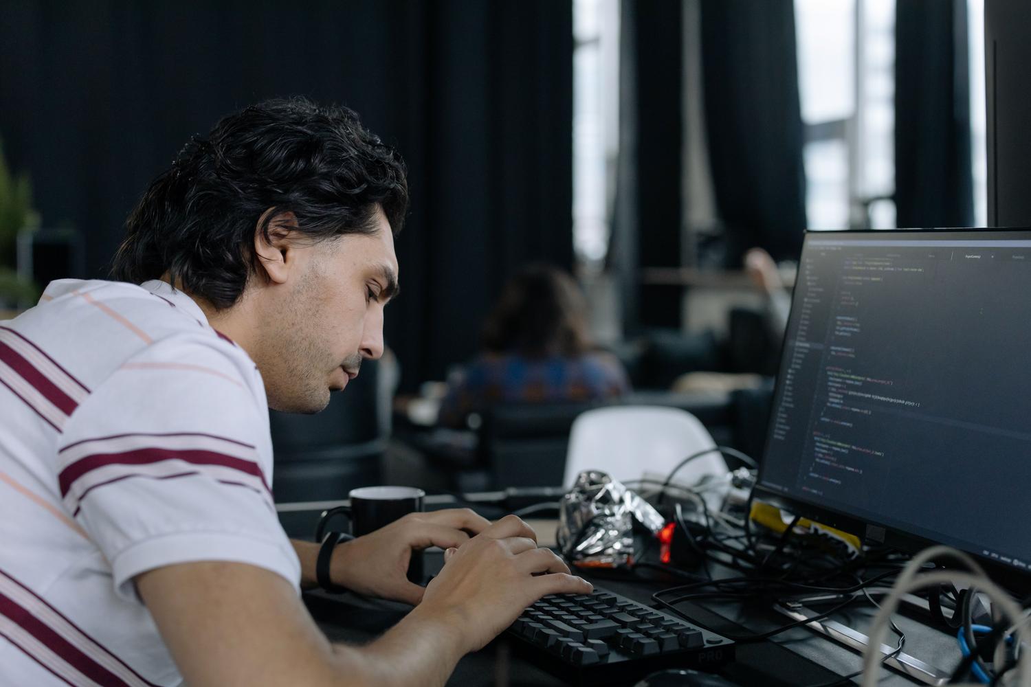 Professional coder intensely typing at a workstation in a contemporary office setup.