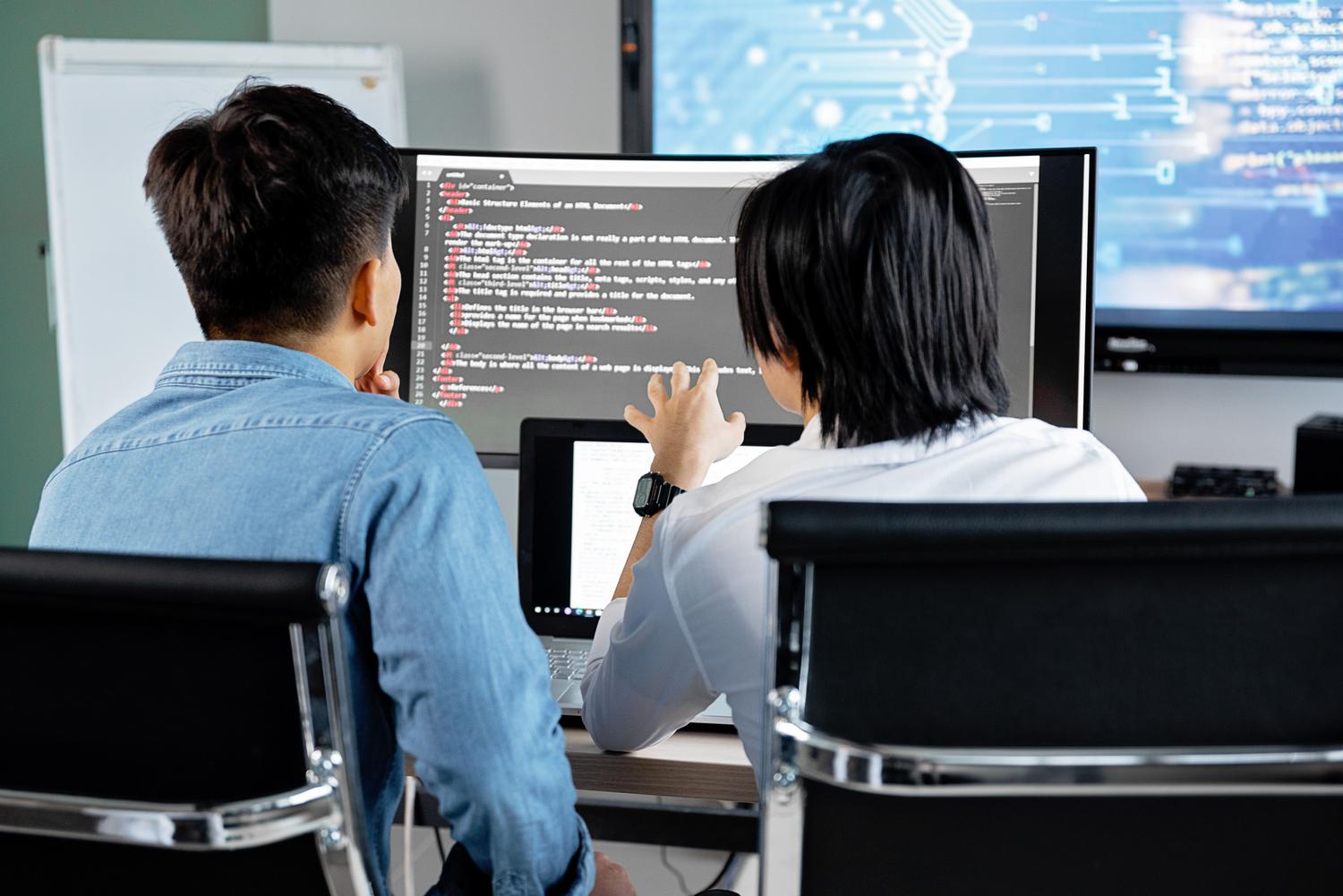 Two developers collaborating and analyzing web code on a monitor in a modern office.