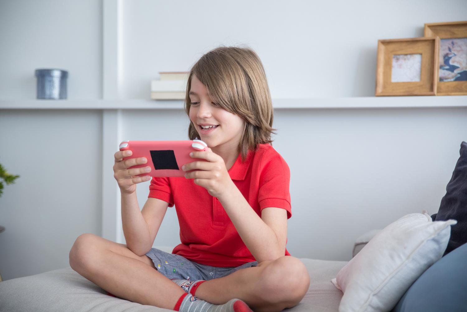 Niño jugando alegremente con un dispositivo portátil en el sofá, representando la accesibilidad móvil de la plataforma Roblox.