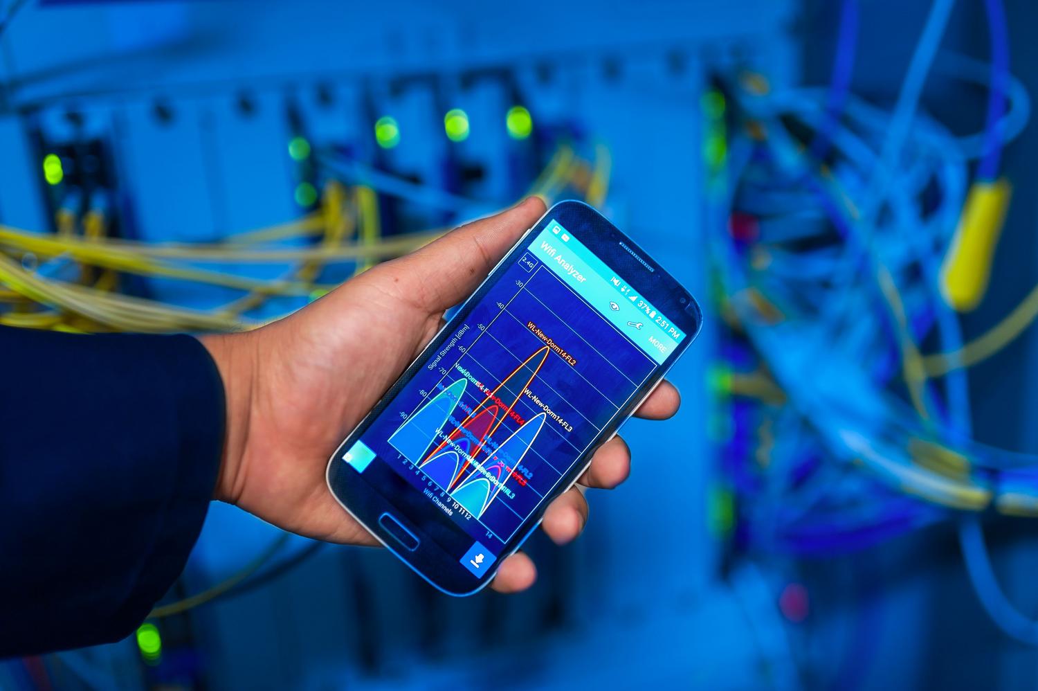 Una persona sosteniendo un smartphone que muestra un análisis de red en un entorno de servidores de alta tecnología, representando el control centralizado y la agilidad de la SDN.