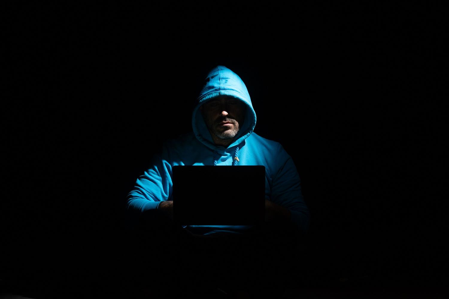 Persona anónima con capucha usando un ordenador portátil en la oscuridad, simbolizando la privacidad digital.