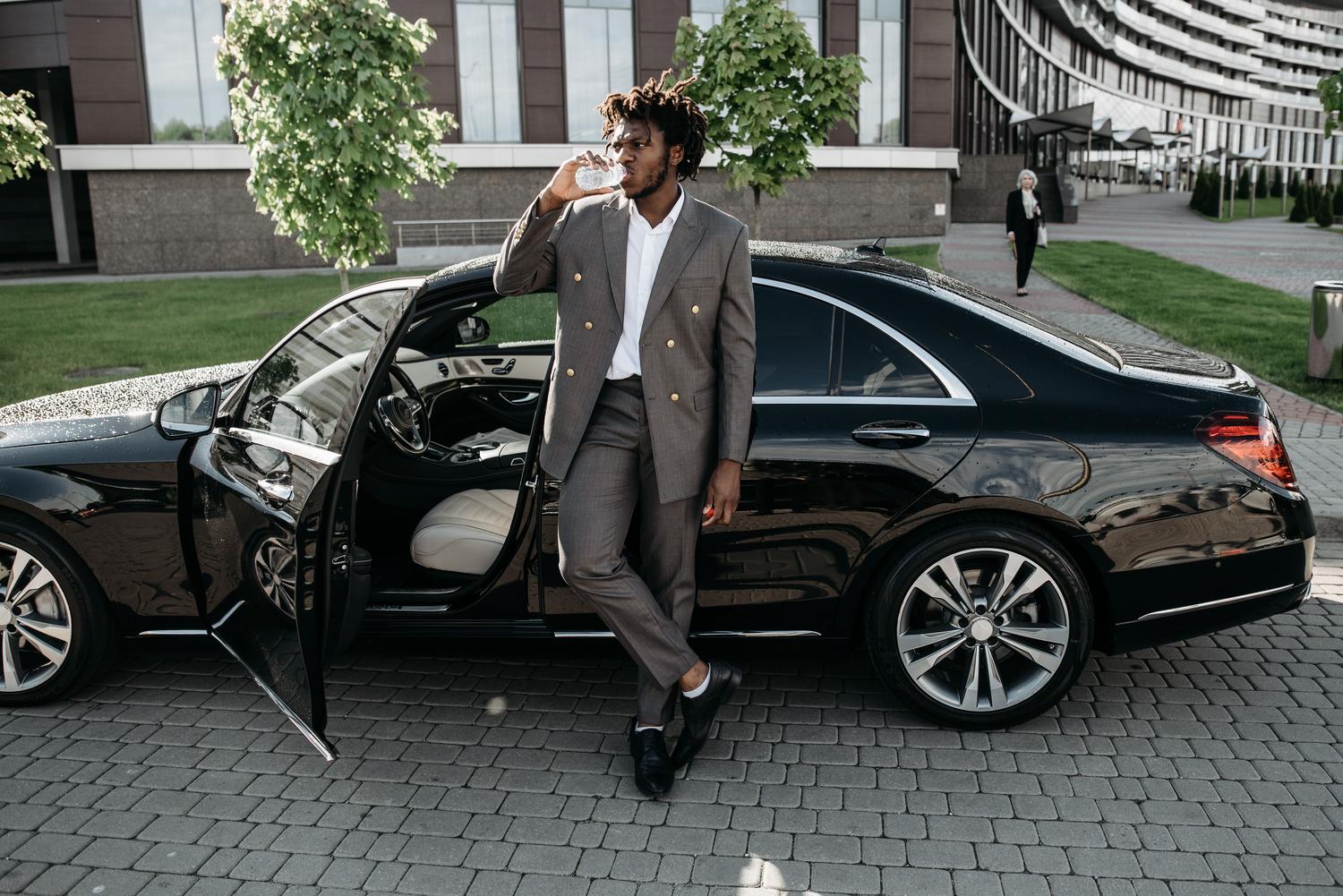 Hombre elegante junto a un coche de lujo en la ciudad, representando el éxito y el prestigio de una organización criminal.