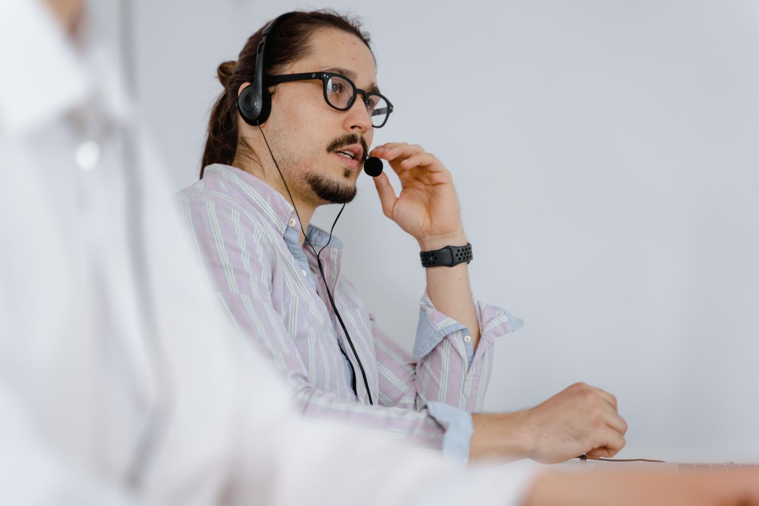 Agente de atención al cliente concentrado utilizando auriculares con micrófono, destacando el toque humano y la dedicación en el soporte omnicanal.