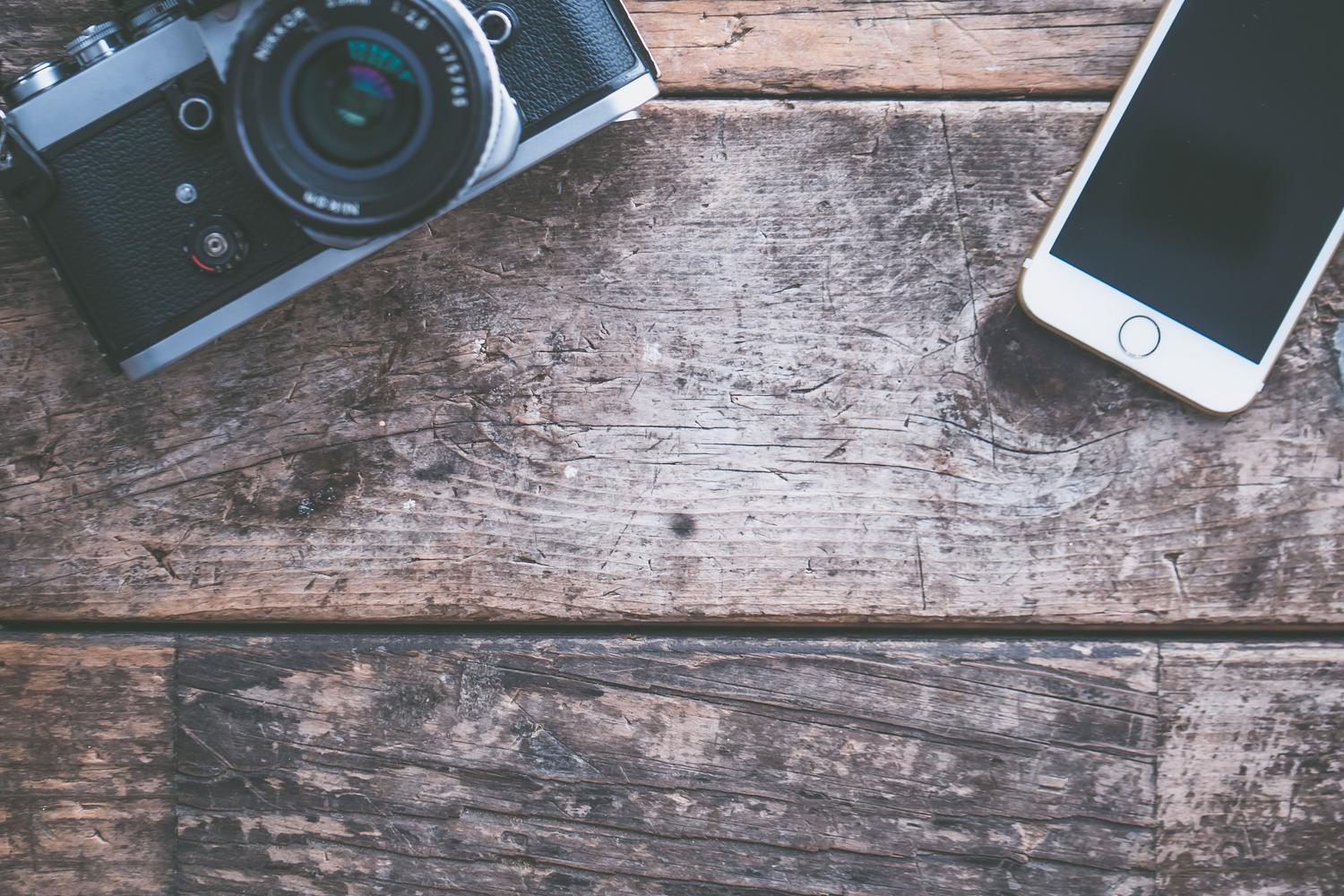 Composición cenital de una cámara fotográfica y un smartphone sobre una mesa de madera, representando la transferencia de fotos inalámbrica.