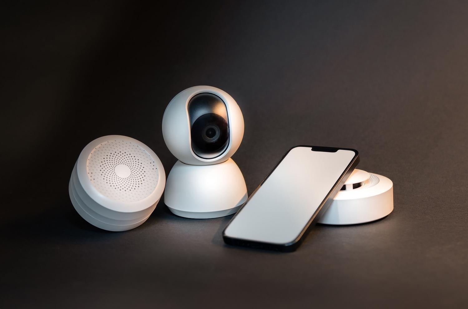 Smartphone y diversos dispositivos de hogar inteligente sobre un fondo minimalista, representando el ecosistema de seguridad.