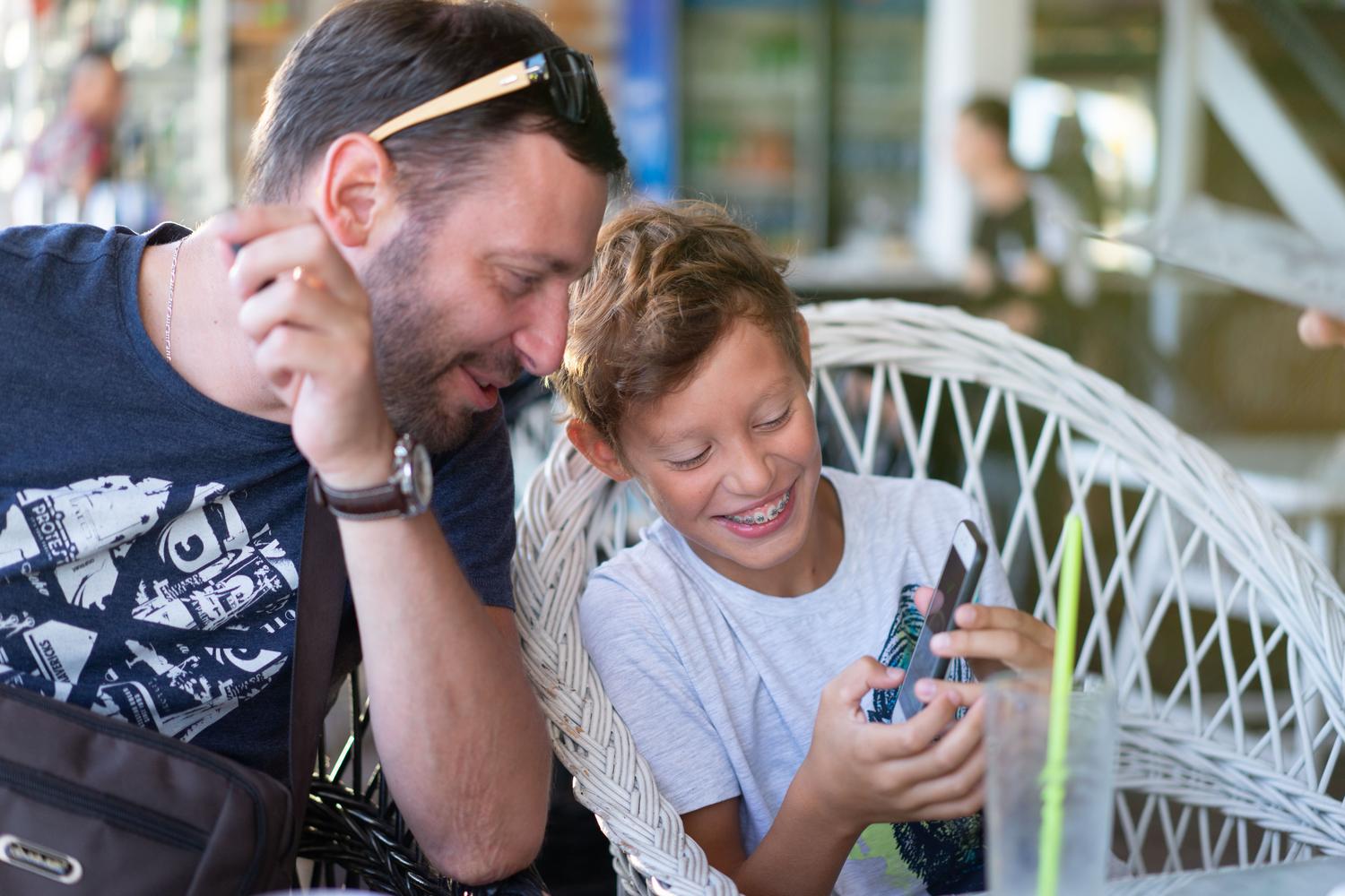 Padre e hijo compartiendo un momento alegre mientras miran un teléfono, ilustrando la importancia del acompañamiento y el diálogo.