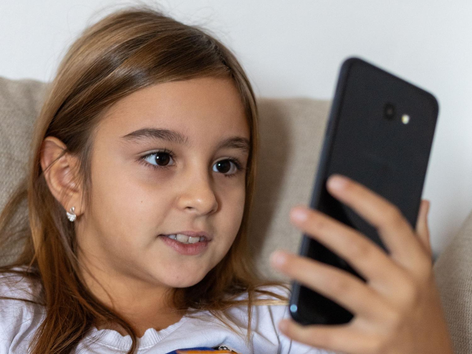 Niña preadolescente utilizando un smartphone en casa, representando el perfil de usuario típico para el control parental.