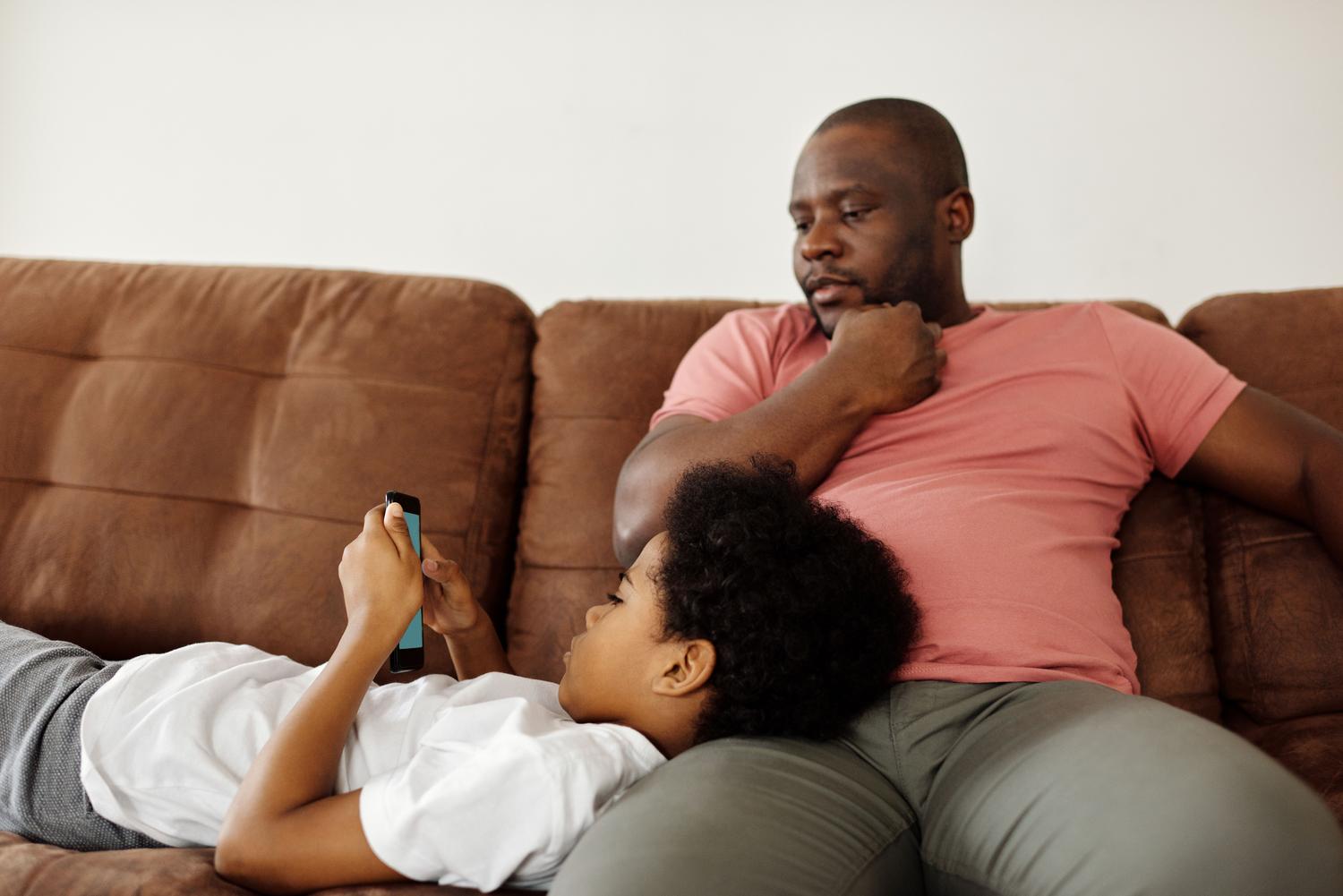 Padre observando discretamente a su hijo mientras este usa el móvil, representando la supervisión parental activa.